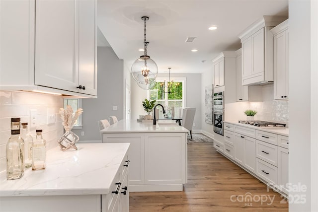 kitchen with a center island with sink, a sink, white cabinetry, tasteful backsplash, and light wood-type flooring