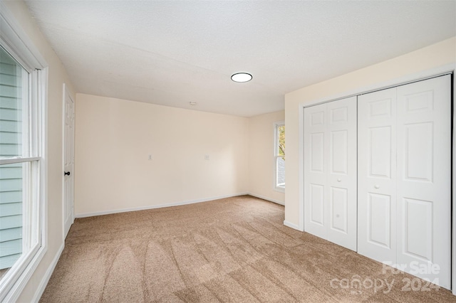 unfurnished bedroom featuring a textured ceiling, light carpet, and a closet