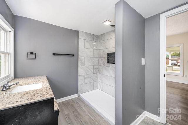 bathroom with hardwood / wood-style floors, tiled shower, a healthy amount of sunlight, and vanity