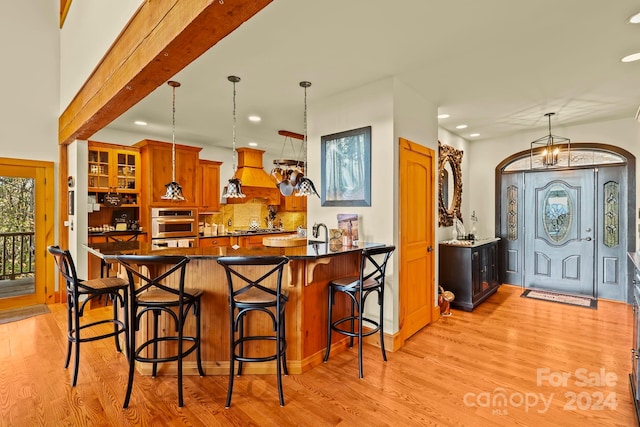 kitchen featuring pendant lighting, light wood-type flooring, oven, and custom exhaust hood