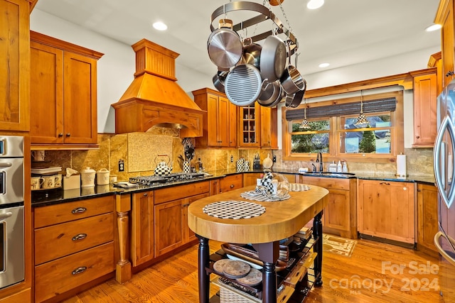 kitchen with dark stone counters, sink, light wood-type flooring, and backsplash