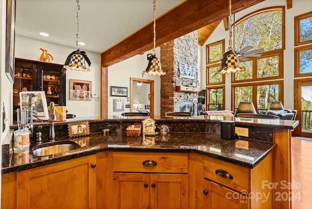 kitchen featuring sink, light wood-type flooring, a fireplace, decorative light fixtures, and dark stone countertops