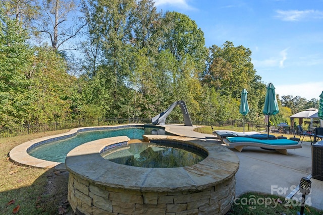 view of pool with a water slide, a patio, and an in ground hot tub