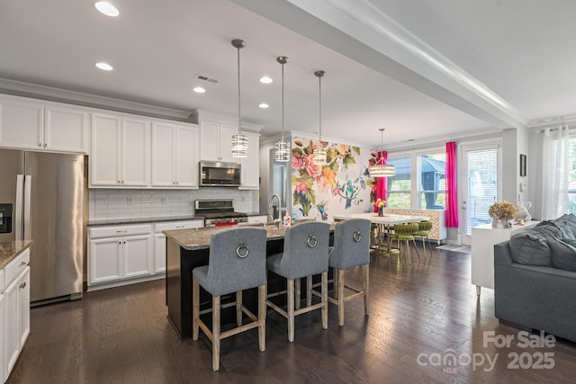 kitchen with pendant lighting, stainless steel appliances, an island with sink, and white cabinets