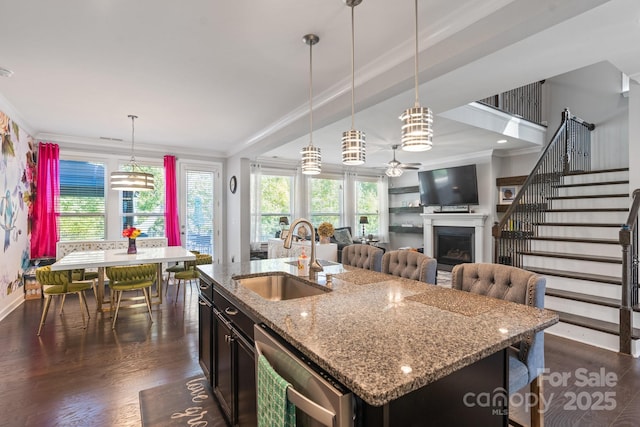 kitchen with decorative light fixtures, an island with sink, sink, ornamental molding, and light stone countertops