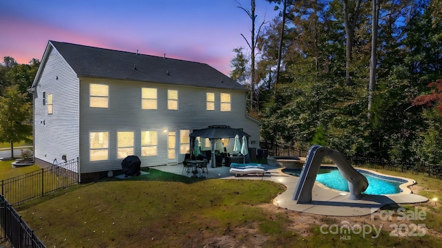 back house at dusk featuring a swimming pool with hot tub, a gazebo, a yard, and a patio area