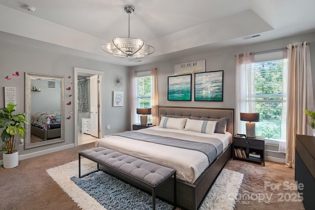 carpeted bedroom with connected bathroom, a chandelier, and a tray ceiling