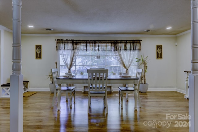 dining room featuring crown molding, a textured ceiling, hardwood / wood-style flooring, and decorative columns