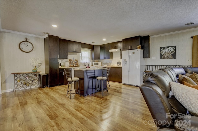 kitchen featuring light hardwood / wood-style floors, dark brown cabinetry, a kitchen bar, and white appliances