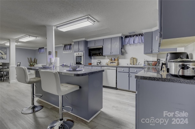 kitchen with stainless steel appliances, a kitchen bar, gray cabinets, a textured ceiling, and light hardwood / wood-style floors