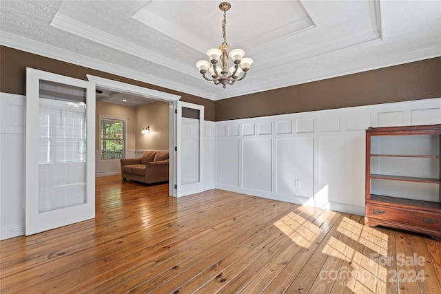 unfurnished dining area featuring crown molding, a tray ceiling, a chandelier, light hardwood / wood-style flooring, and a textured ceiling