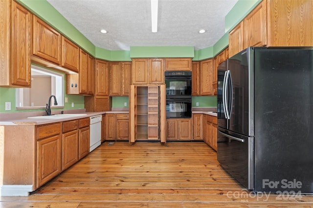 kitchen featuring a textured ceiling, light wood-type flooring, sink, and black appliances