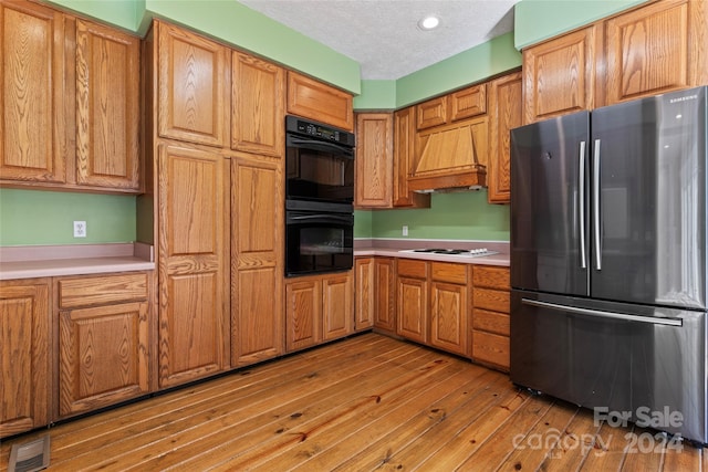 kitchen with a textured ceiling, black double oven, stainless steel fridge, and light hardwood / wood-style flooring