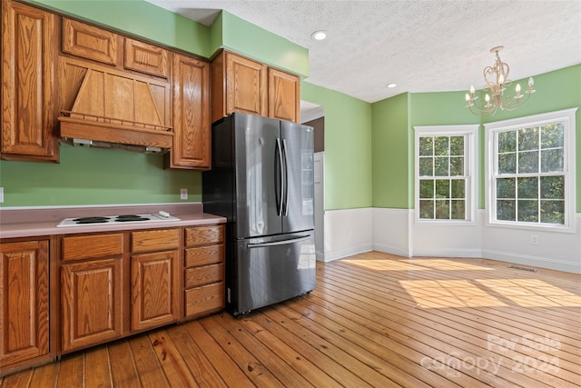 kitchen with hanging light fixtures, light hardwood / wood-style flooring, stainless steel fridge, and custom range hood