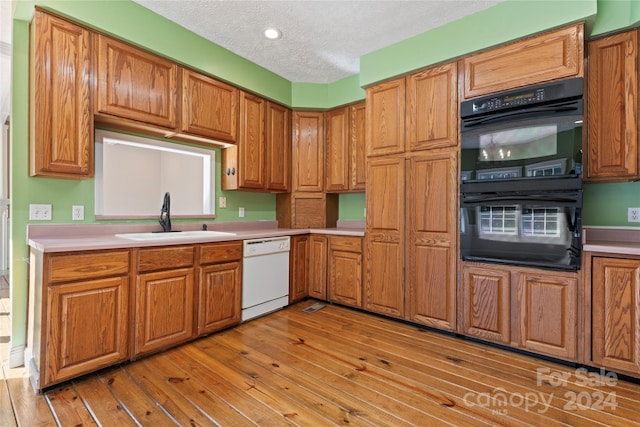 kitchen featuring dishwasher, double oven, light hardwood / wood-style flooring, and a textured ceiling