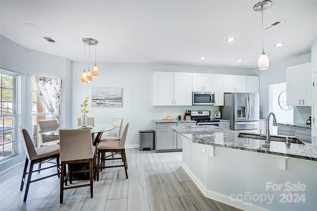 kitchen with sink, appliances with stainless steel finishes, decorative light fixtures, white cabinets, and light wood-type flooring