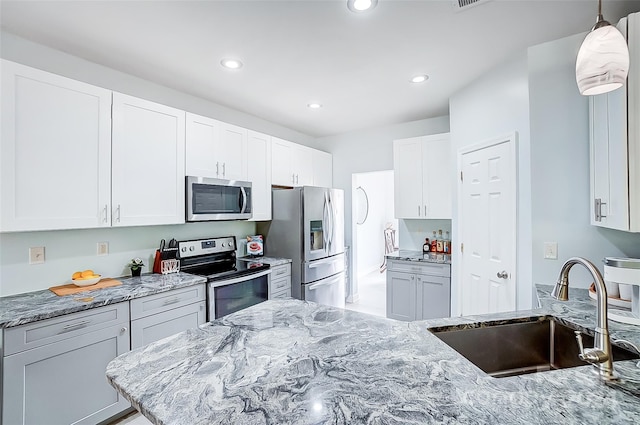 kitchen with light stone counters, white cabinetry, appliances with stainless steel finishes, hanging light fixtures, and sink