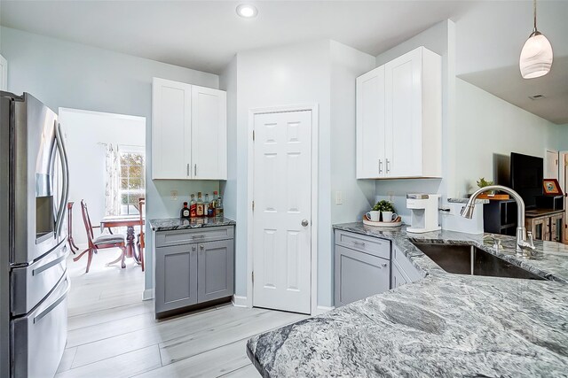 kitchen featuring hanging light fixtures, stainless steel refrigerator with ice dispenser, sink, and white cabinets