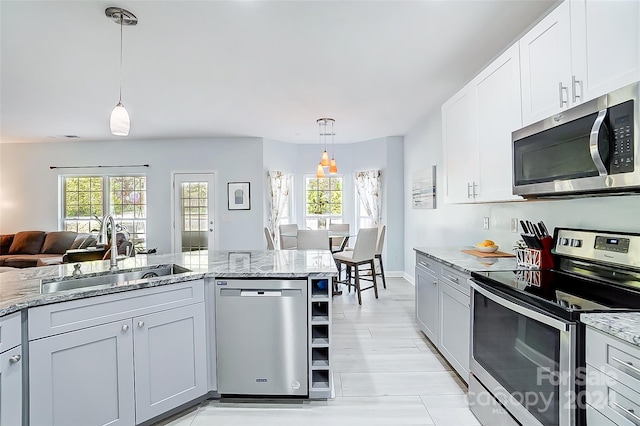 kitchen with appliances with stainless steel finishes, light stone countertops, hanging light fixtures, sink, and white cabinets