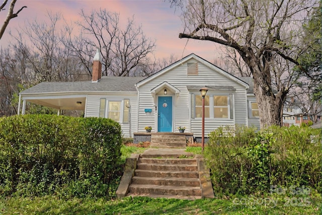 view of front of house featuring a shingled roof, an attached carport, and a chimney