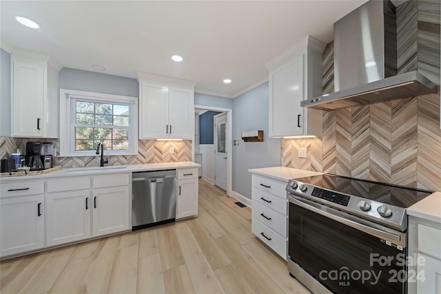 kitchen featuring light wood-type flooring, decorative backsplash, stainless steel appliances, wall chimney range hood, and white cabinetry