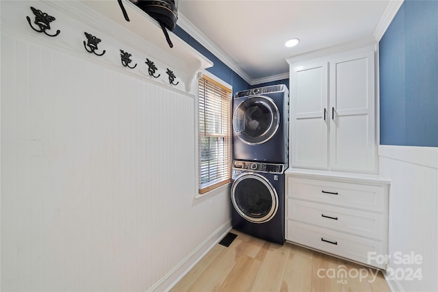 clothes washing area with cabinets, light hardwood / wood-style flooring, ornamental molding, and stacked washing maching and dryer