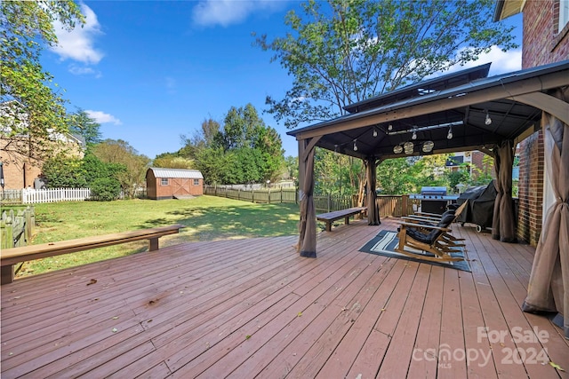 wooden terrace featuring a gazebo, a yard, a storage unit, and grilling area