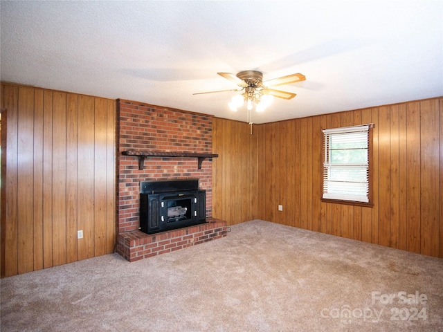 unfurnished living room featuring a fireplace, ceiling fan, wood walls, and carpet