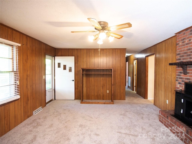 unfurnished living room featuring a wood stove, ceiling fan, wood walls, and light colored carpet