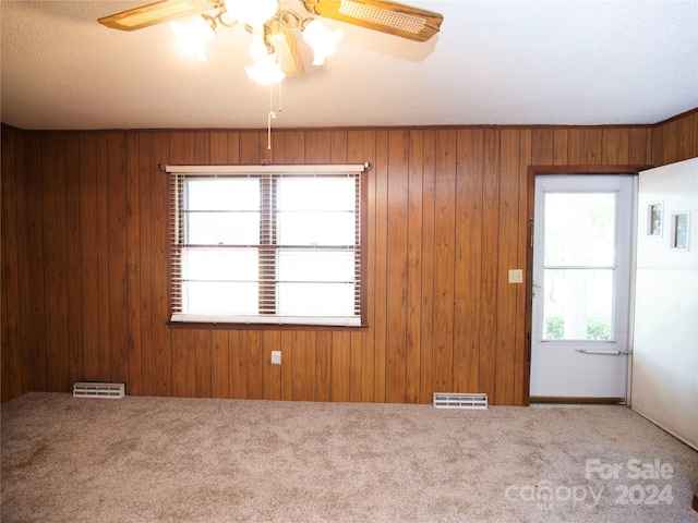 empty room with carpet flooring, wooden walls, and ceiling fan