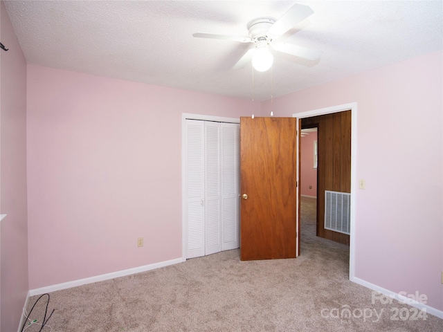 unfurnished bedroom with ceiling fan, a textured ceiling, a closet, and light carpet