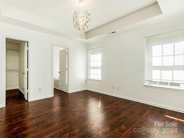 unfurnished bedroom with ensuite bathroom, dark hardwood / wood-style floors, a tray ceiling, and an inviting chandelier