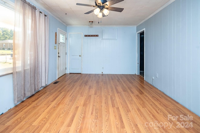 empty room featuring ceiling fan, wood walls, light wood-type flooring, and crown molding