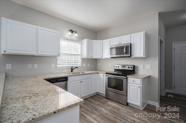 kitchen featuring sink, white cabinetry, hardwood / wood-style flooring, appliances with stainless steel finishes, and light stone countertops