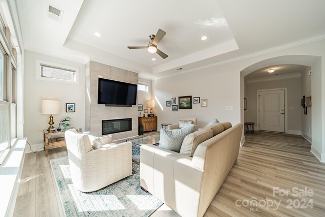 living room with a tray ceiling, ornamental molding, light hardwood / wood-style flooring, and a fireplace