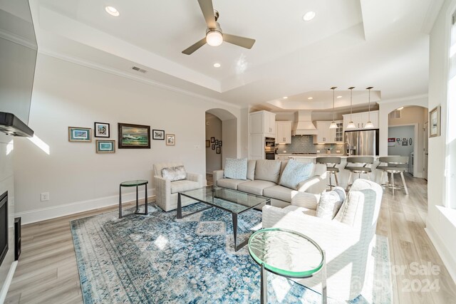 living room featuring light hardwood / wood-style flooring, ornamental molding, a tray ceiling, and ceiling fan