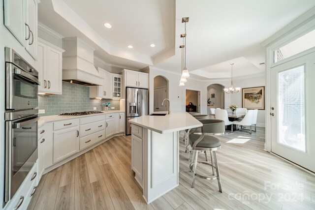 kitchen featuring a raised ceiling, sink, an island with sink, and white cabinets