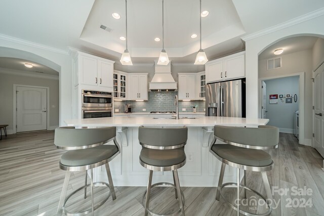 kitchen featuring custom exhaust hood, white cabinets, a raised ceiling, pendant lighting, and stainless steel appliances