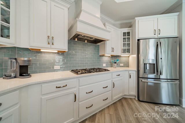 kitchen featuring white cabinetry, custom range hood, stainless steel appliances, and light wood-type flooring