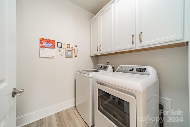 laundry room featuring washing machine and clothes dryer, light hardwood / wood-style floors, and cabinets