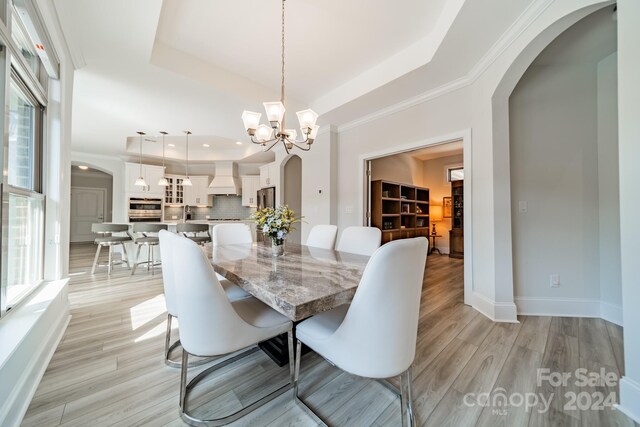 dining area featuring ornamental molding, light hardwood / wood-style flooring, an inviting chandelier, and a raised ceiling