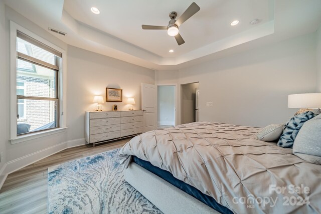 bedroom featuring ceiling fan, a raised ceiling, multiple windows, and light hardwood / wood-style floors