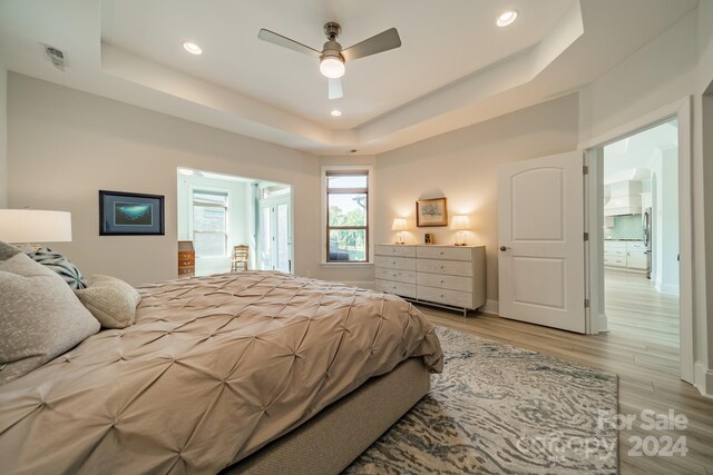 bedroom featuring light hardwood / wood-style flooring, a tray ceiling, and ceiling fan