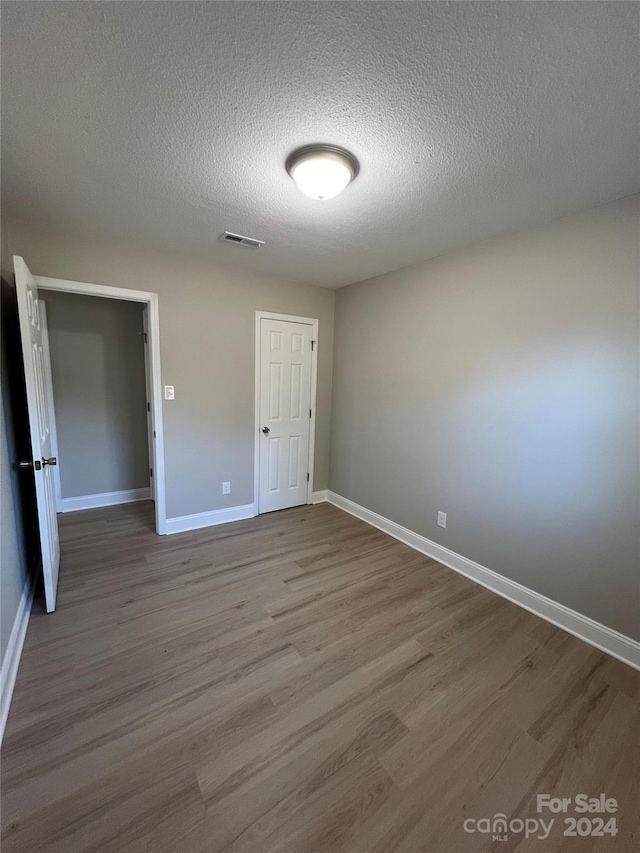 unfurnished bedroom featuring a closet, a textured ceiling, and hardwood / wood-style flooring