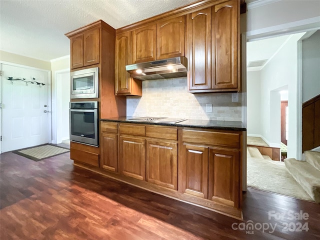 kitchen with backsplash, stainless steel appliances, dark wood-type flooring, ornamental molding, and a textured ceiling