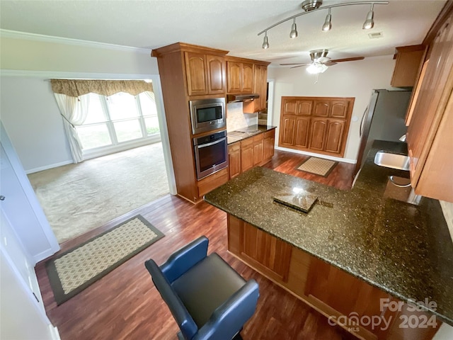 kitchen featuring ceiling fan, dark stone countertops, dark wood-type flooring, ornamental molding, and appliances with stainless steel finishes