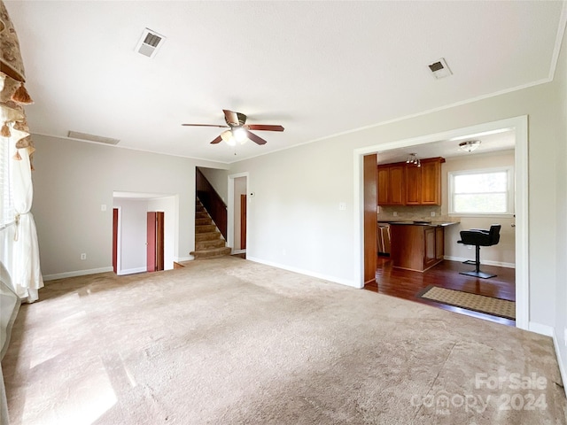 unfurnished living room featuring ceiling fan, light colored carpet, and ornamental molding