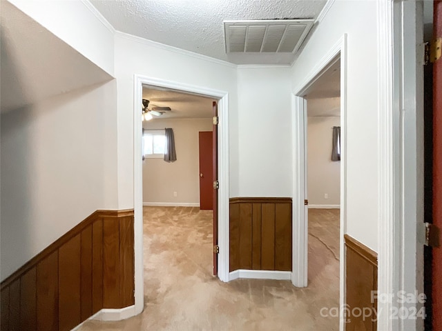 corridor with light carpet, a textured ceiling, wood walls, and ornamental molding