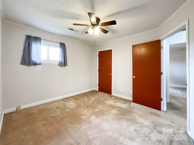 unfurnished bedroom featuring ornamental molding, ceiling fan, a textured ceiling, and light colored carpet