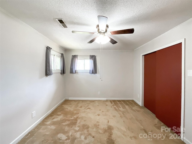 unfurnished bedroom with ceiling fan, a textured ceiling, a closet, light carpet, and crown molding